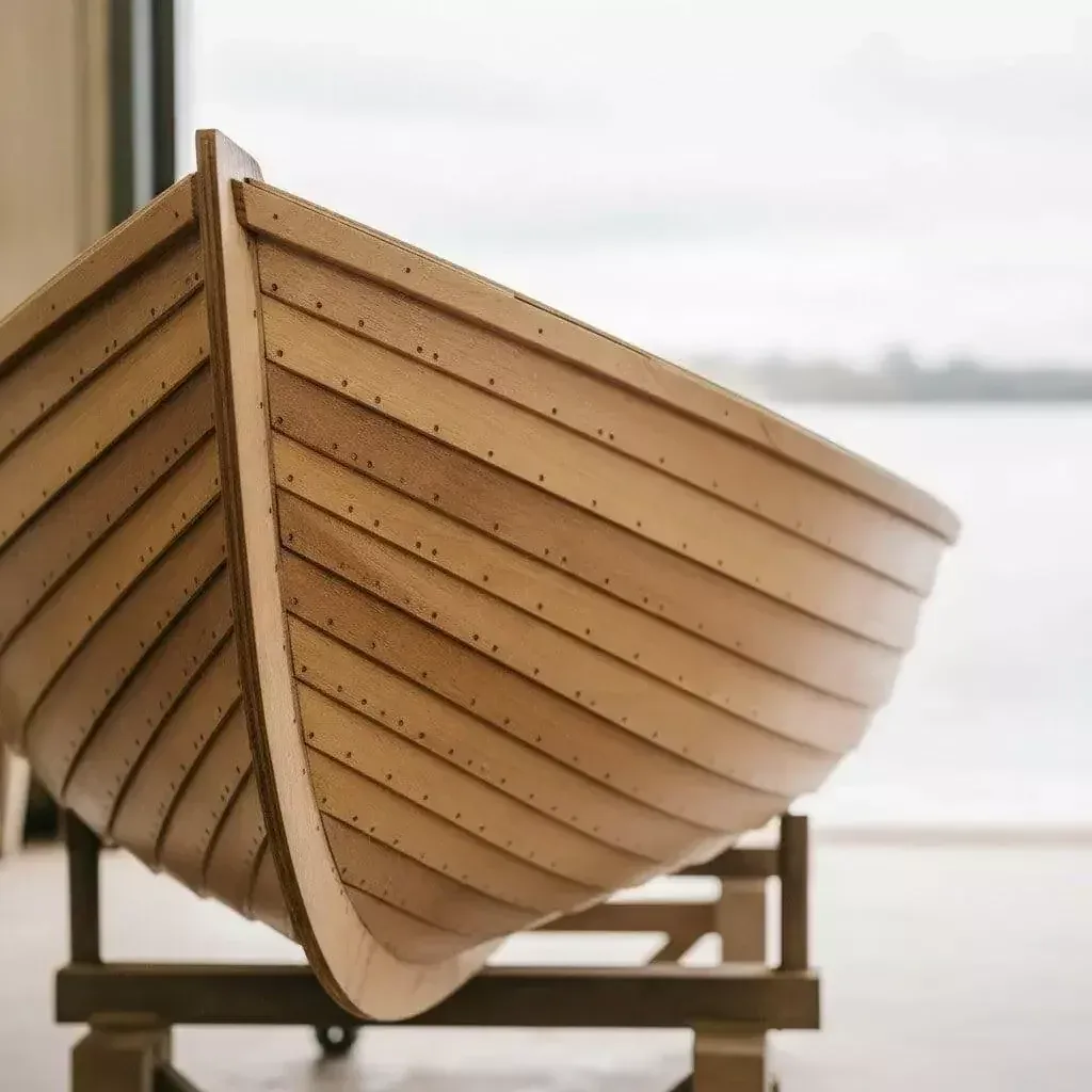 Clinker-built wooden boat hull on a cradle beside open water